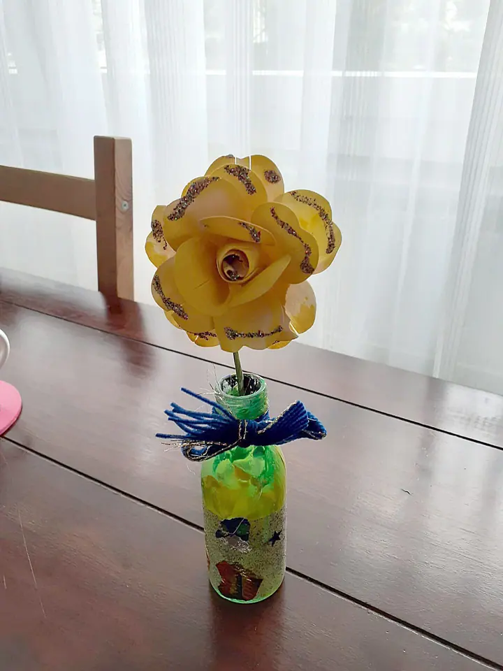 Gebastelte gelbe Papierblume in einer verzierten Flasche