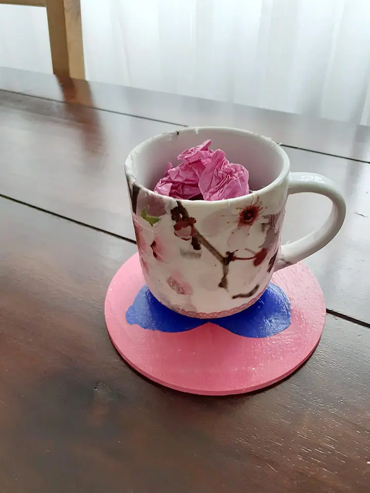 Bemalte Tasse mit Seidenpapier-Blüten auf einem rosa Untersetzer