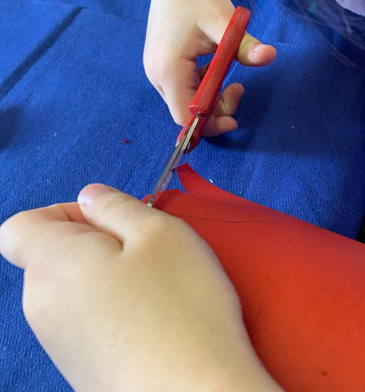 Kinderhände schneiden mit einer roten Schere Papier auf blauem Filz